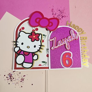 Puede incluir: Un adorno para tarta de cumpleaños con un diseño de Hello Kitty. El adorno incluye un lazo rosa, la figura de Hello Kitty, el nombre "Zayah", el número "6" y las palabras "Happy Birthday". El fondo es rosa y blanco.
