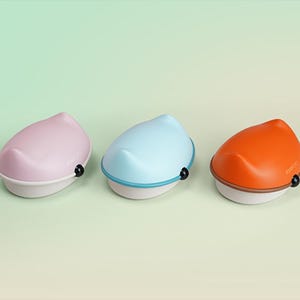 Puede incluir: Tres jaboneras con forma de gato en rosa, azul y naranja. Cada jabonera tiene una base blanca, un borde a juego y un botón negro. Las jaboneras están dispuestas sobre un fondo verde claro.