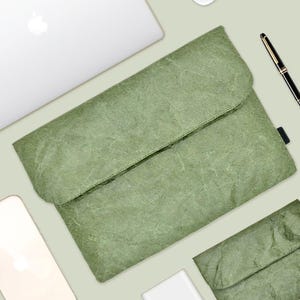 May include: A green, textured, paper-like laptop sleeve with a fold-over flap. The sleeve is made of a durable, water-resistant material and is perfect for protecting your laptop from scratches and bumps.