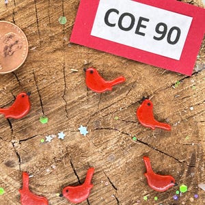May include: Red glass bird figurines on a wooden surface with a red card that says "COE 90".