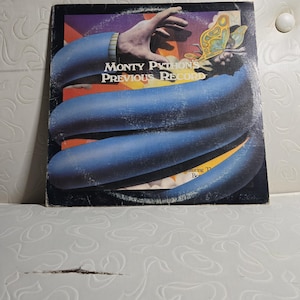 May include: A vintage vinyl record album cover featuring a blue and orange abstract design with a hand reaching towards a butterfly. The album title is "Monty Python's Previous Record".