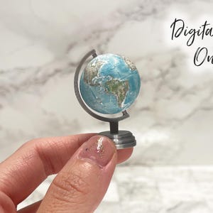 May include: A miniature globe on a grey stand featuring a detailed map of the Earth with blue oceans and green and brown landmasses. The text Digital File Only is printed in black script in the upper right corner of the image.