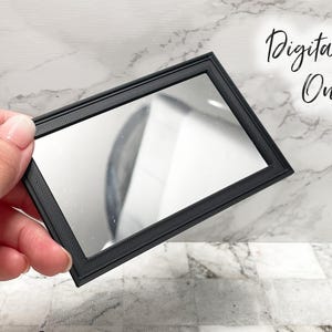 May include: A small, rectangular black mirror with a textured frame is held in a hand. The mirror reflects a blurry image. The words "Digital File Only" are written in cursive in the upper right corner.