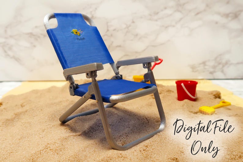 May include: A blue and silver folding beach chair with a floral design on the back. The chair is sitting on a sandy surface. "Digital File Only" is written on the sand.