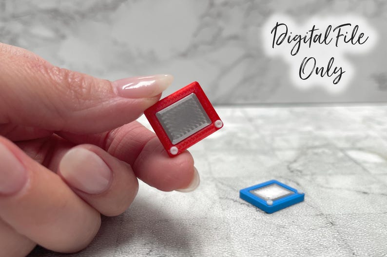 May include: Miniature red Etch-A-Sketch toy with a silver screen and white knobs. A blue version of the toy is also visible. The image includes the text "Digital File Only".