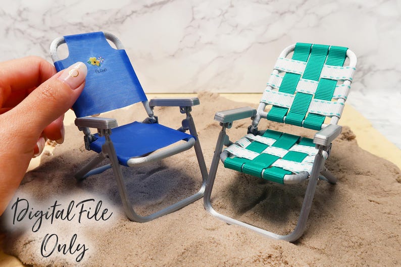 May include: Two miniature folding beach chairs, one blue and one green, on a sandy surface. The blue chair has a floral design on the back.