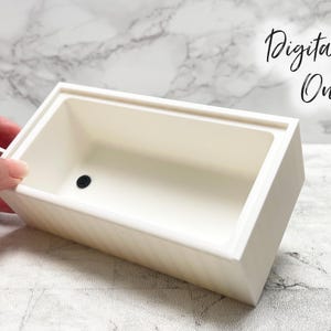 Peut inclure: Un récipient rectangulaire blanc cassé avec un point noir au centre. Le récipient est tenu par une main et a un extérieur texturé. Le texte "Digital File Only" est écrit en cursive en arrière-plan.