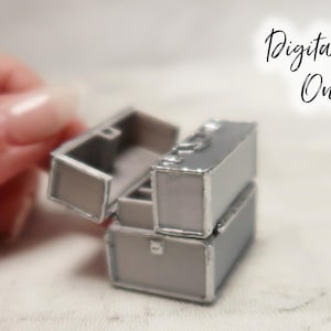 Puede incluir: Tres maletas plateadas apiladas con una maleta superior ligeramente abierta. Las maletas son de color gris claro con ribetes plateados. El texto "Archivo digital solamente" es visible en el fondo.