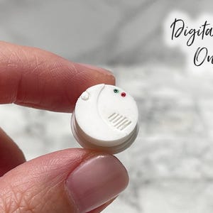 Puede incluir: Un pequeño detector de humo blanco con luces indicadoras rojas y verdes. El dispositivo tiene un diseño circular con una serie de rejillas horizontales y el texto "Digital File Only" en el fondo.