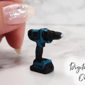 Może przedstawiać: Miniaturowy, bezprzewodowy wiertarko-wkrętarka w kolorze czarnym i niebieskim z srebrnym wiertłem. Wiertarko-wkrętarka jest wielkości paznokcia.