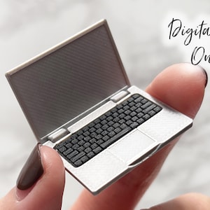 以下が含まれることがあります： 黒いキーボードと画面を備えた、ミニチュアのシルバーのラップトップ。 ラップトップは指の間に保持されています。 「Digital File Only」というテキストが右上隅にイタリック体で書かれています。 本物のラップトップのミニチュア版です。