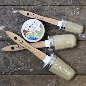 May include: A set of paint brushes and brush soap. The brushes have light wood handles with the word "mint" printed on them. The brush soap container features a retro illustration of a woman flexing her arm and the words "Get Minted!" printed on it.
