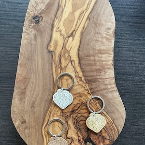 Peut inclure: Trois porte-clés en forme de cœur avec un motif en spirale. Les porte-clés sont argentés, dorés et bronze et sont présentés sur une surface en bois.