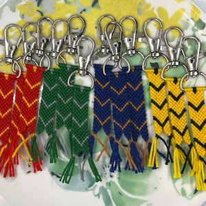 May include: Set of five colourful keychains with woven tassels and silver key rings. The tassels are red and yellow, green and grey, blue and gold, yellow and black.