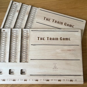 May include: A wooden board game titled "THE TRAIN GAME" with engraved train tracks and train symbols. Includes multiple wooden game pieces and a storage box. The game board features the "GYRA Designs" logo and numbers 1 to 21.