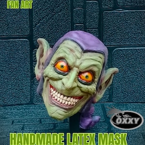 May include: Green and purple latex mask of the Green Goblin from the Spider-Man comics. The mask has a wide, toothy grin and large, orange eyes. The mask is handmade and is labeled "HANDMADE LATEX MASK".