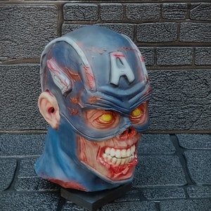 May include: A blue and red zombie Captain America mask with a cracked and weathered appearance. The mask has a large 'A' on the forehead and yellow eyes. The mouth is open and shows teeth.