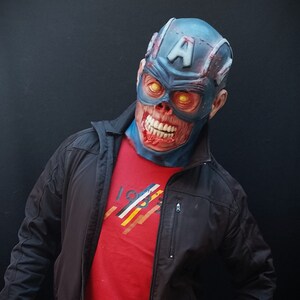 May include: A person wearing a blue and red zombie Captain America mask with a black jacket and red shirt. The shirt has a graphic design with the number 1983.