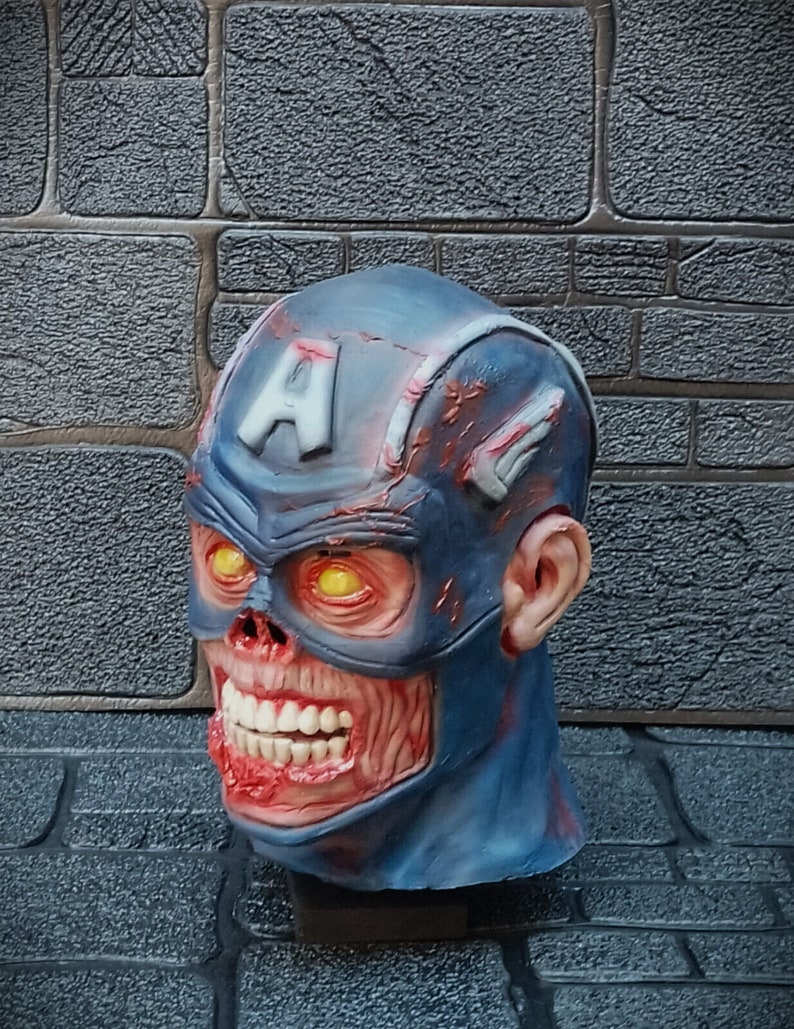 May include: A blue and red zombie Captain America mask with glowing yellow eyes. The mask is made of plastic and has a detailed design.