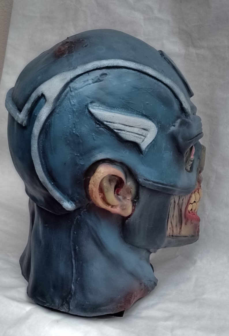May include: A blue and white zombie Captain America Halloween mask. The mask is made of latex and has a detailed design. The mask has a distressed look with visible cracks and tears.