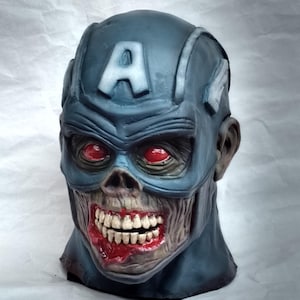 May include: A blue and gray zombie Captain America mask with a red, white, and blue 'A' on the forehead. The mask has red eyes and a bloody, open mouth with teeth.