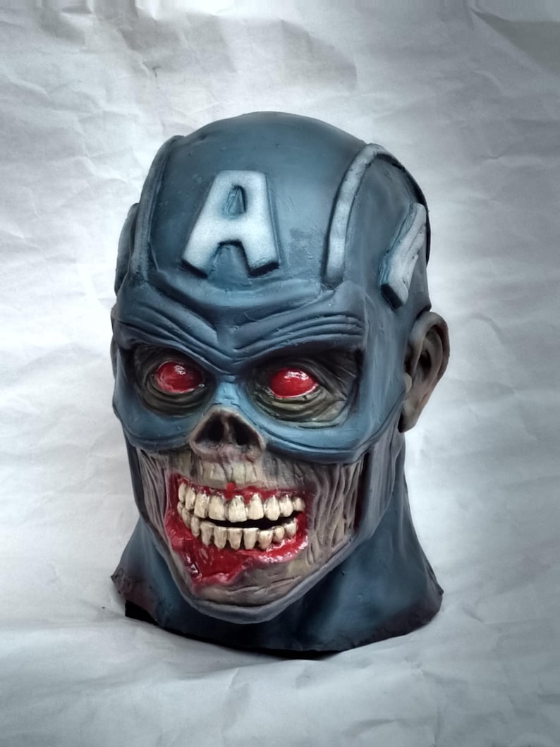 May include: A blue and gray zombie Captain America mask with a red, white, and blue 'A' on the forehead. The mask has red eyes and a bloody, open mouth with teeth.