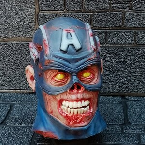 May include: A blue and red zombie Captain America mask with a white 'A' on the forehead. The mask has a gruesome, bloody appearance with exposed teeth and yellow eyes.