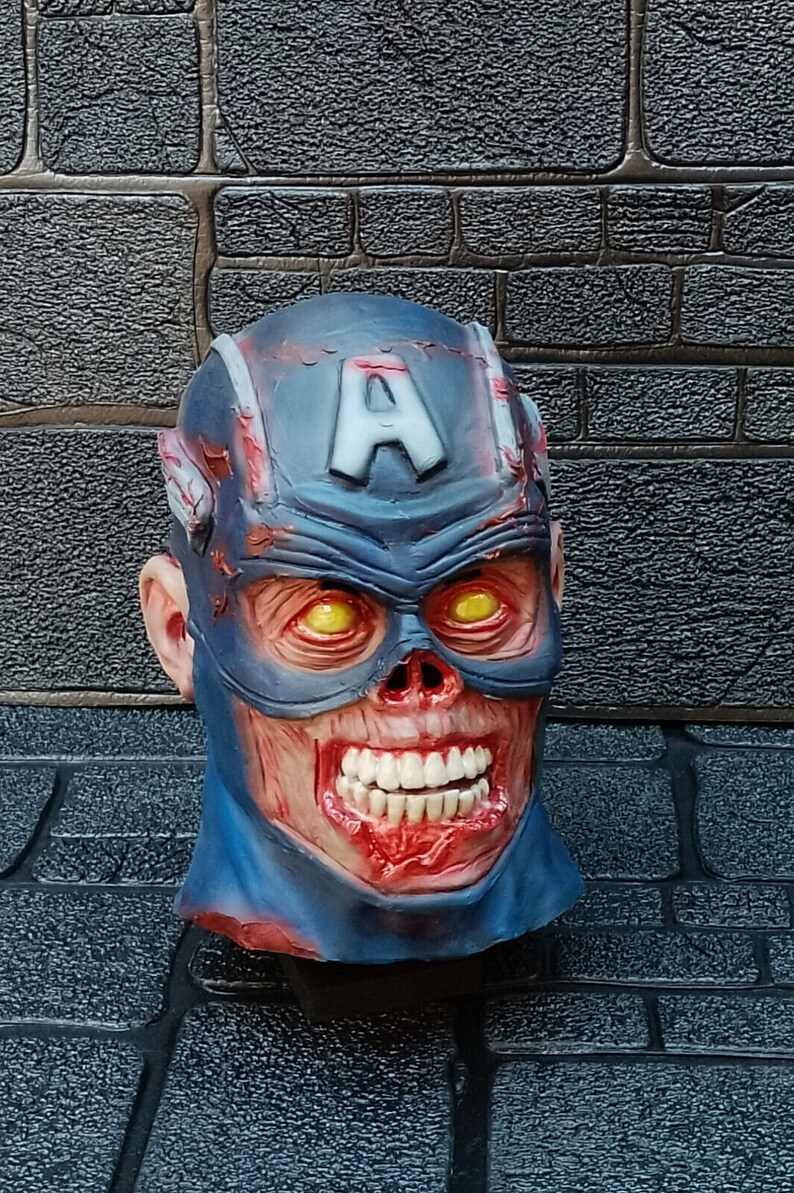 May include: A blue and red zombie Captain America mask with a white 'A' on the forehead. The mask has a gruesome, bloody appearance with exposed teeth and yellow eyes.