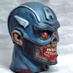May include: A blue and white zombie Captain America mask with red eyes. The mask is made of plastic and has a detailed sculpt of a zombie face.