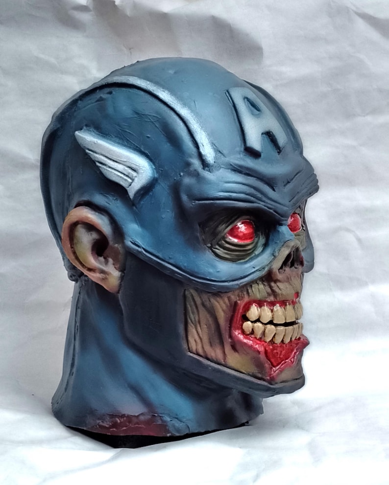 May include: A blue and white zombie Captain America mask with red eyes. The mask is made of plastic and has a detailed sculpt of a zombie face.