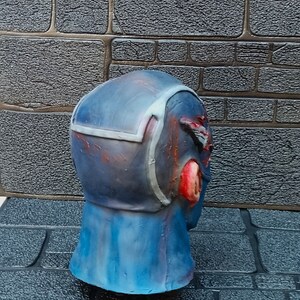 May include: A blue and red painted, detailed, plastic mask with a textured surface. The mask is a head-sized, realistic depiction of a human head.
