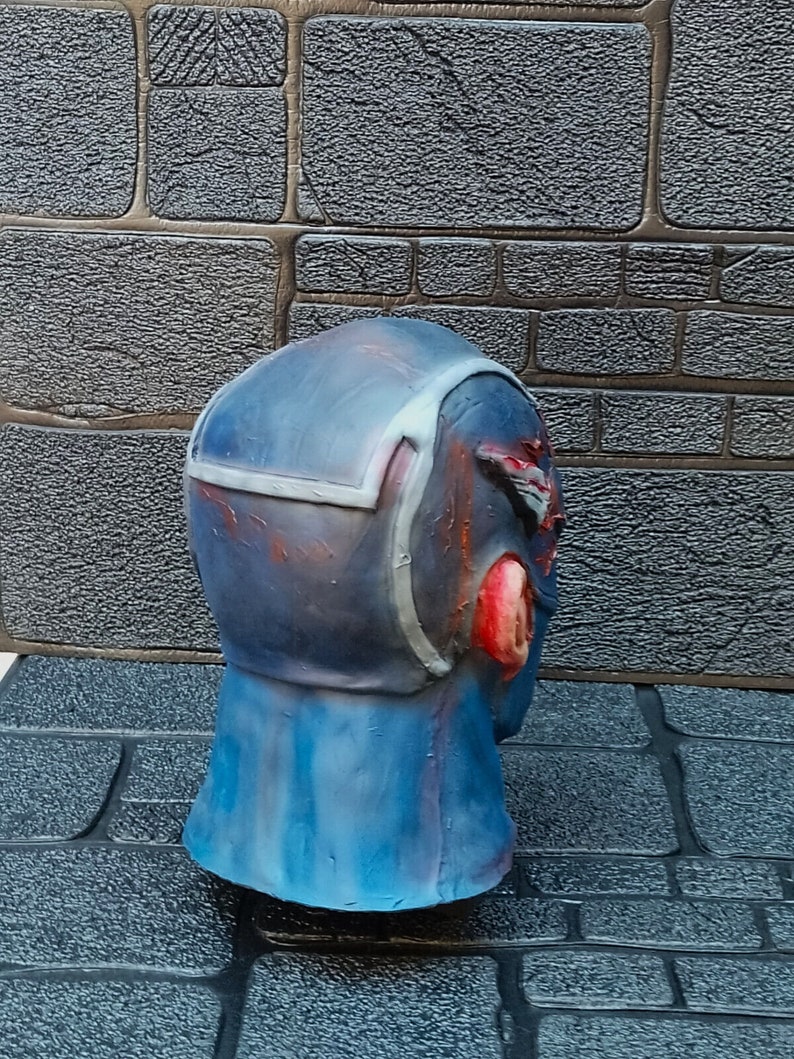 May include: A blue and red painted, detailed, plastic mask with a textured surface. The mask is a head-sized, realistic depiction of a human head.