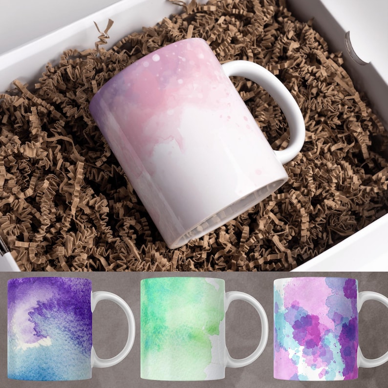 May include: Three ceramic mugs with watercolor designs. The mugs are white with a handle and feature abstract watercolor designs in shades of purple, green, and pink.
