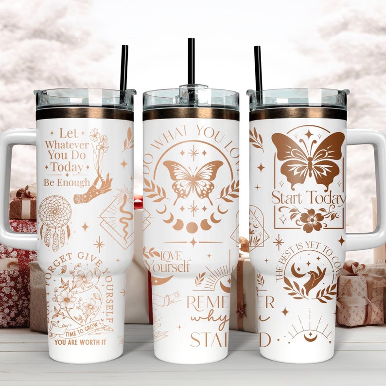 Puede incluir: Tres vasos de acero inoxidable blanco con detalles en oro rosa y frases inspiradoras. Los vasos presentan dise&ntilde;os de mariposas, fases lunares y otros s&iacute;mbolos celestiales. Las frases incluyen "Haz lo que amas", "Comienza hoy" y "Deja que todo lo que hagas hoy sea suficiente".