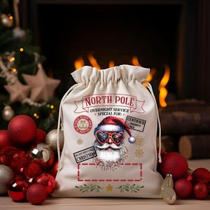 Puede incluir: Un saco de Santa de lona blanca con una ilustraci&oacute;n de Santa Claus rojo y blanco con gafas de sol. El saco tiene el texto "North Pole Overnight Service Special For:" y "Certified Naughty Nice" impreso en &eacute;l.