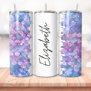 Puede incluir: Tres vasos de acero inoxidable con un dise&ntilde;o de escamas de sirena. El vaso del medio es blanco con el nombre "Elizabeth" escrito en cursiva negra. Los vasos de la izquierda y la derecha tienen un dise&ntilde;o de escamas de sirena morado y azul con detalles de purpurina.