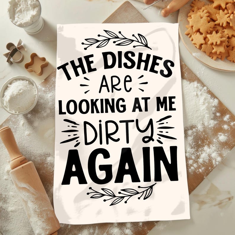 Puede incluir: Toalla de cocina blanca con texto negro que dice "The dishes are looking at me dirty again". El texto est&aacute; rodeado por un dise&ntilde;o floral negro.