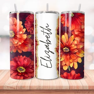 Puede incluir: Tres vasos de acero inoxidable con un dise&ntilde;o floral. El vaso del centro es blanco con detalles de purpurina dorada y el nombre "Elizabeth" escrito en cursiva negra. Los vasos a cada lado presentan un patr&oacute;n floral rojo y naranja.