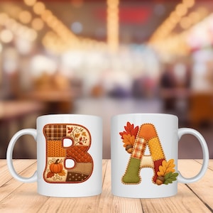 May include: Two white ceramic mugs featuring large, colorful letters. The left mug displays a letter B with a patchwork design of autumn-themed patterns, including a pumpkin. The right mug features a letter A decorated with fall leaves and acorns.