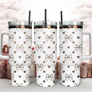 Pu&ograve; includere: Tre bicchieri in acciaio inossidabile bianco con coperchio e cannuccia dorati. I bicchieri presentano un motivo di fiocchi e cuori marroni.