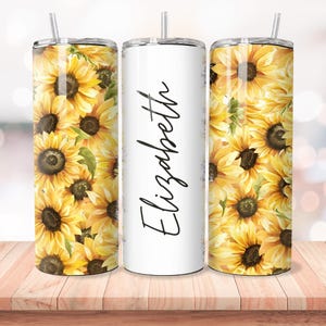 Puede incluir: Tres vasos de acero inoxidable con un dise&ntilde;o de girasol. El vaso del medio es blanco con el nombre "Elizabeth" escrito en cursiva negra.