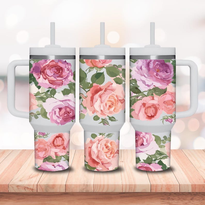 May include: Three stainless steel tumblers with a floral design. The tumblers are white with a silver lid and a straw. The floral design features pink and white roses on a light blue background.