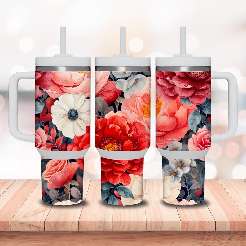 May include: Three stainless steel tumblers with a floral design. The tumblers are white with a silver lid and a straw. The floral design features red, pink, and white flowers on a dark background.