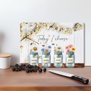May include: A white wooden cutting board with a floral design and the text "Today I choose". Four mason jars with flowers and the words "Faith", "Hope", "Love", and "Joy" are arranged on the board.