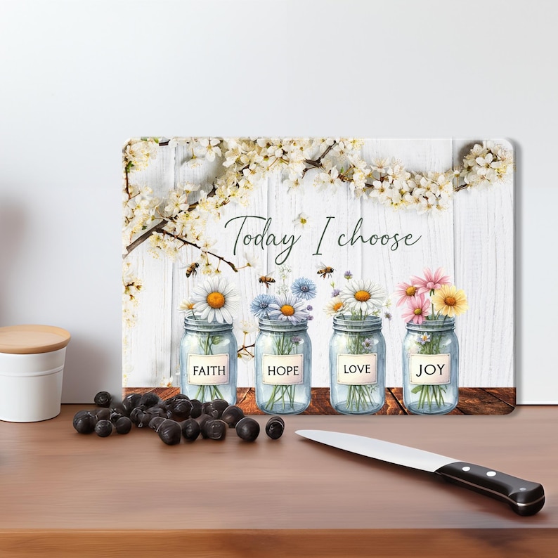 May include: A white wooden cutting board with a floral design and the text "Today I choose". Four mason jars with flowers and the words "Faith", "Hope", "Love", and "Joy" are arranged on the board.