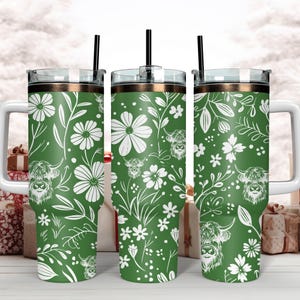 May include: Three green stainless steel tumblers with a white floral and highland cow pattern. The tumblers have lids and straws.
