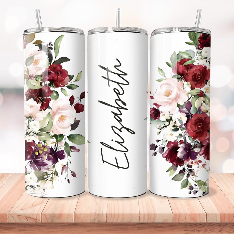 Puede incluir: Tres vasos de acero inoxidable blanco con un dise&ntilde;o floral. El dise&ntilde;o presenta flores de color burdeos, rosa y blanco con hojas verdes. El vaso del medio tiene el nombre "Elizabeth" escrito en cursiva negra.