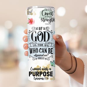 May include: A white tumbler with a blue and gold design. The tumbler features the text "If God is for us, who can be against us?" with bible verses from Romans 8:31 and Ephesians 2:10. The tumbler also features the text "I can do all things through Christ who gives me strength" with the bible verse Philippians 4:13.