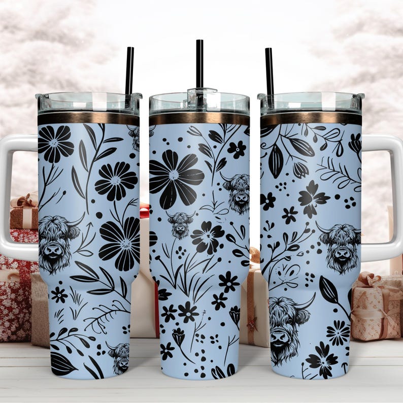 May include: Three stainless steel tumblers with lids and straws. The tumblers are light blue with a black floral pattern and black highland cow silhouettes.