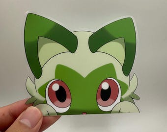 May include: A sticker depicting a cartoon cat with green and white fur, large red eyes, and green ears. The cat is peeking over an edge, creating a playful design. The sticker is likely made of vinyl or a similar material.